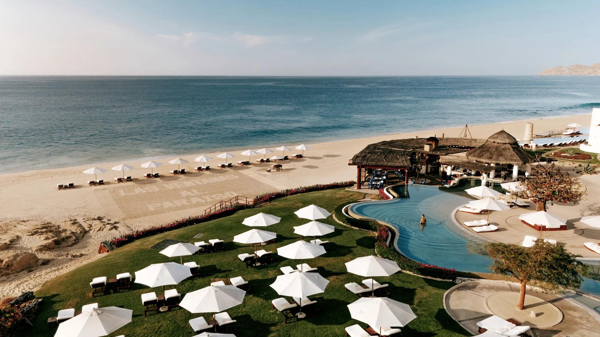 Infinity pool overlooking a white sandy beach, with green grass and lounge beds along the shore