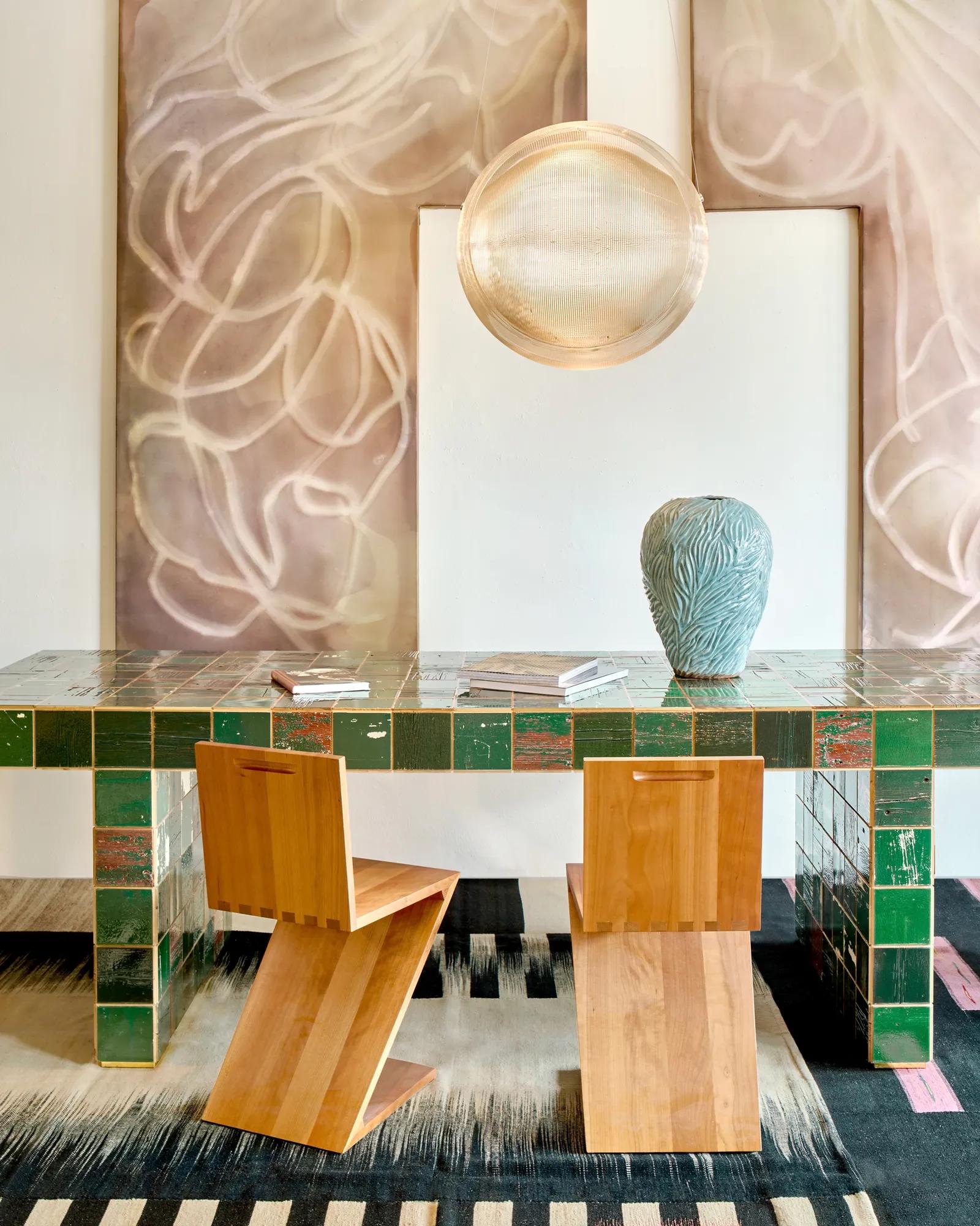 Modern design furniture including wooden chairs, green tiled table, pendant orb light and beige artwork in background 