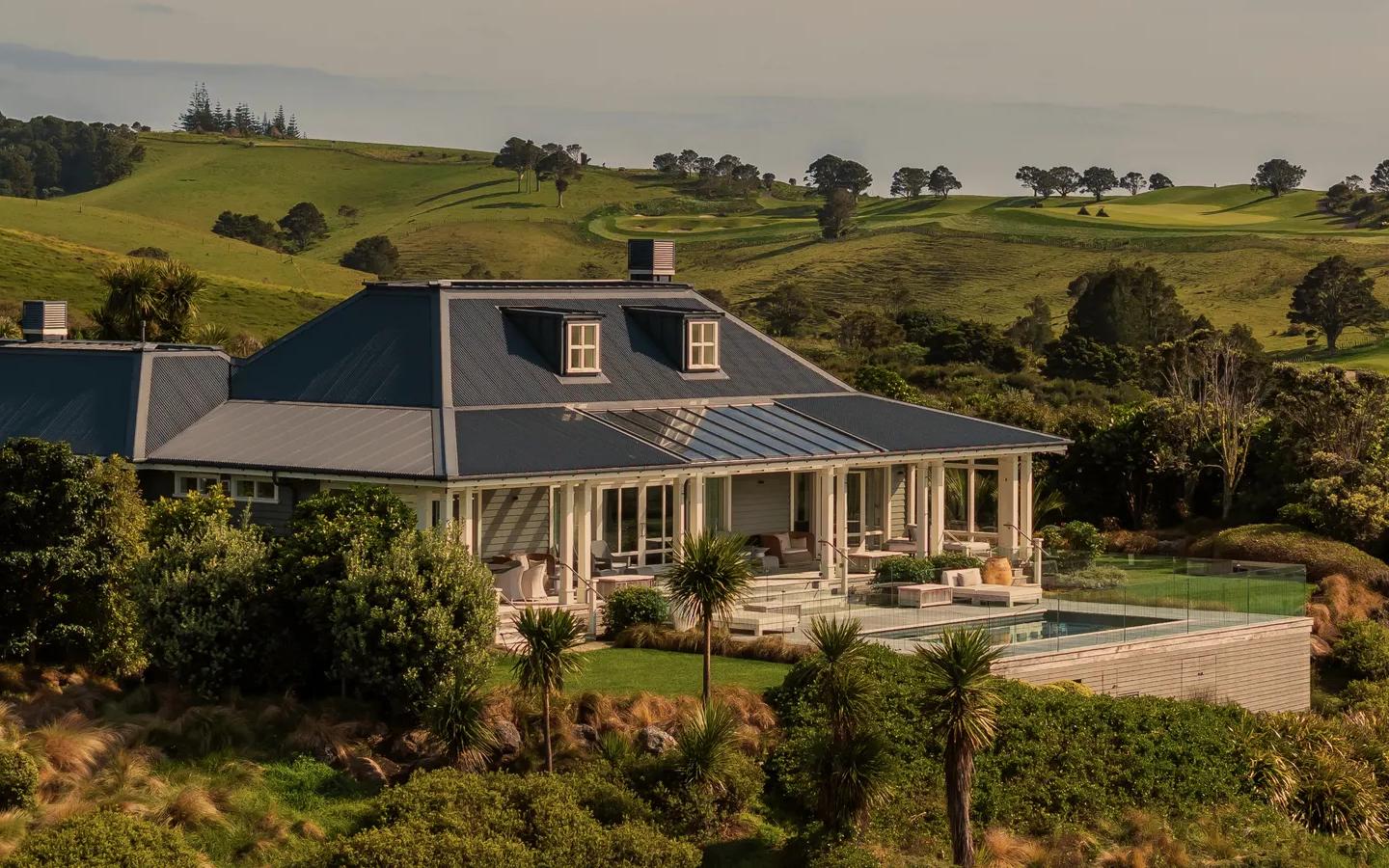 Looking at the Kauri Cliffs Four Bedroom Villa from afar, focus is on the outdoor pool, front terrace and surrounding native landscaping.