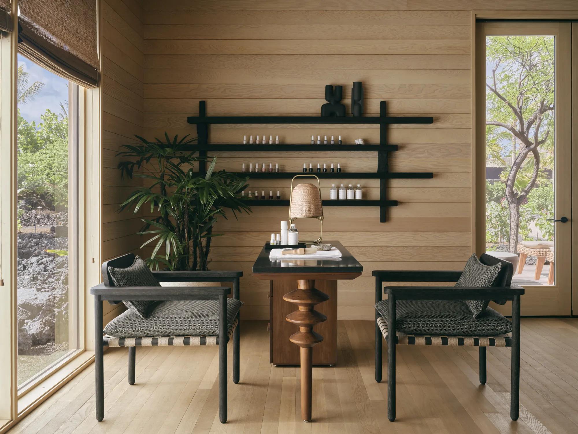 A modern light wood paneled salon with natural light and two chairs on opposite sides of a manicure table and nail polish bottles on a rack on the wall.