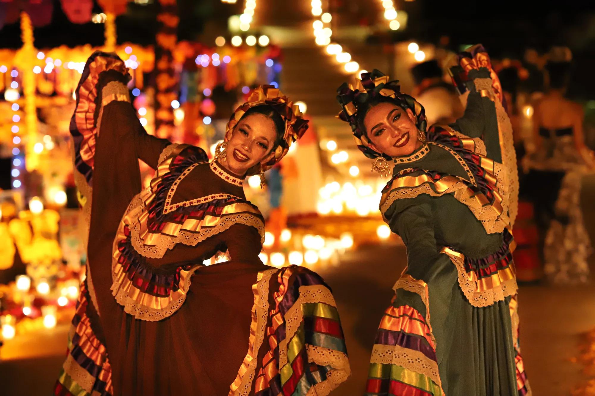 Dia de los Muertos celebration with two women dressed in traditional Mexican dress surrounded by candles and handcrafted Mexican designs