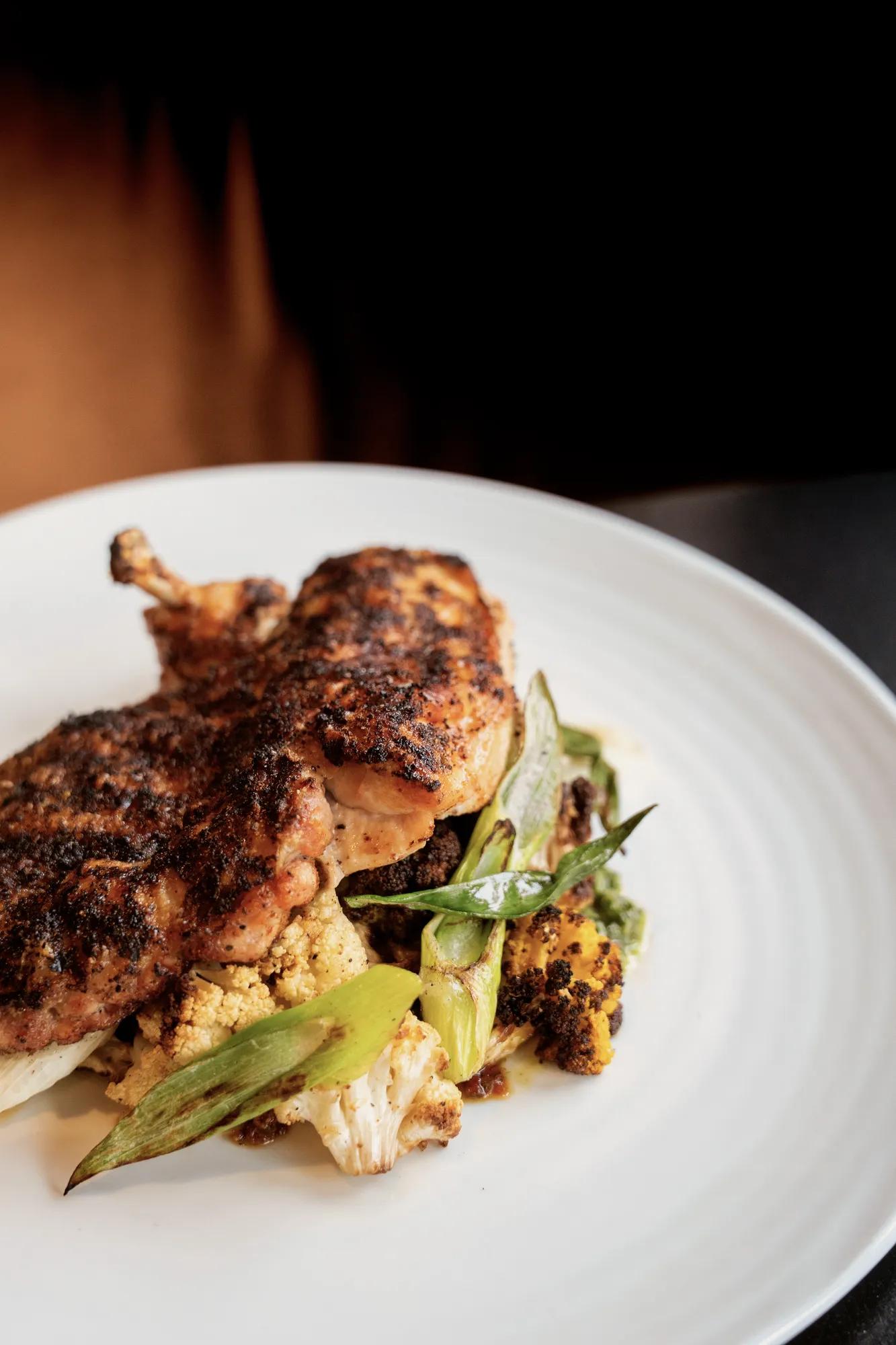Grilled Half Amish chicken plated with vegetables on a white plate with a brown background