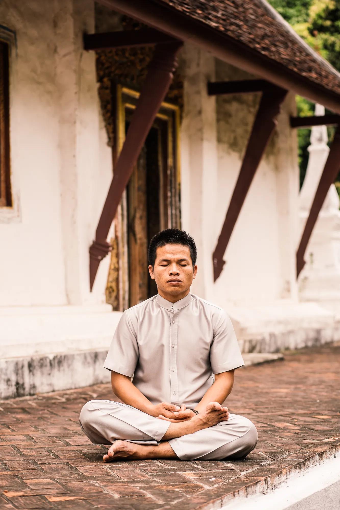 Man meditating in lotus position outside a traditional Southeast Asian temple.