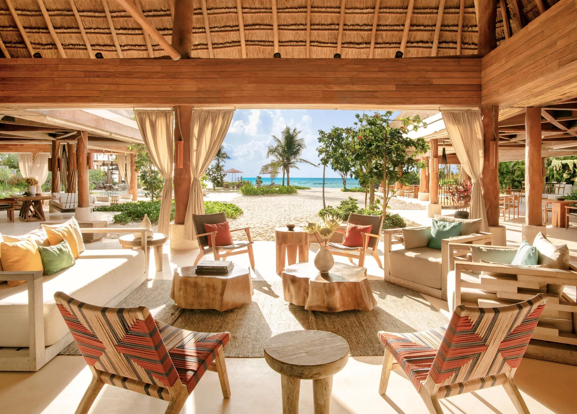 Rosewood Mayakoba - An open-air lounge looking out over the beach through palm trees