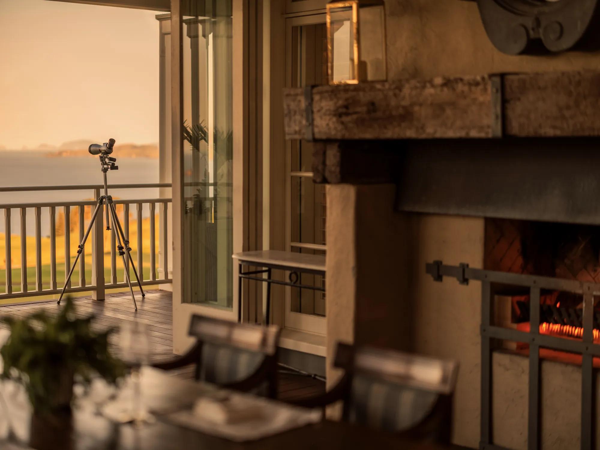 Outdoor dining on the covered Green Room Balcony at Rosewood Kauri Cliffs, with an open fire an panoramic views of the Pacific Ocean.