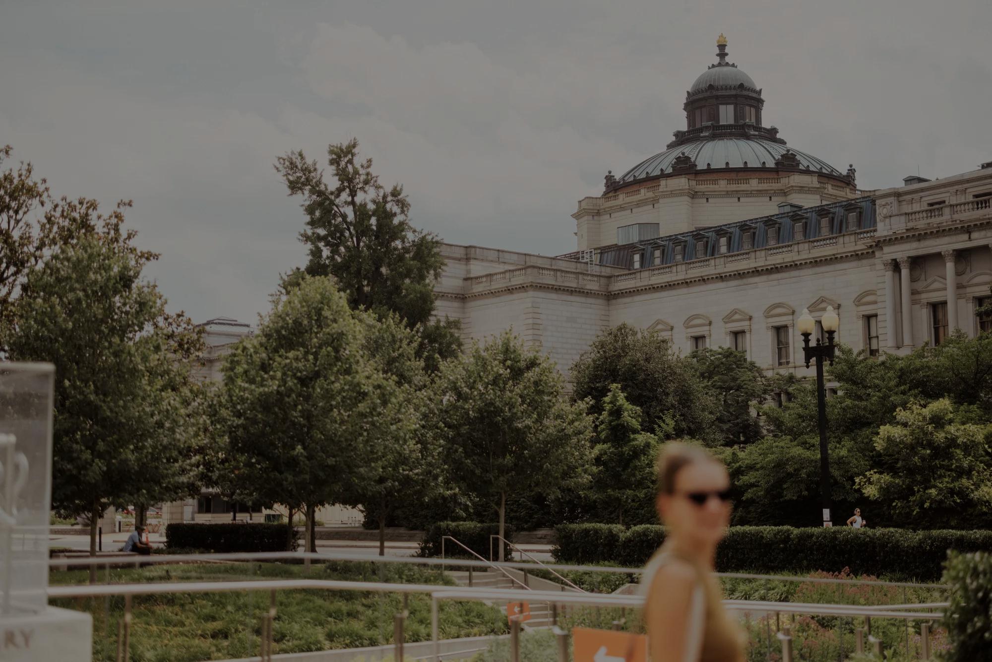 United States Botanical Gardens exterior with a woman blurred walking in front of it.