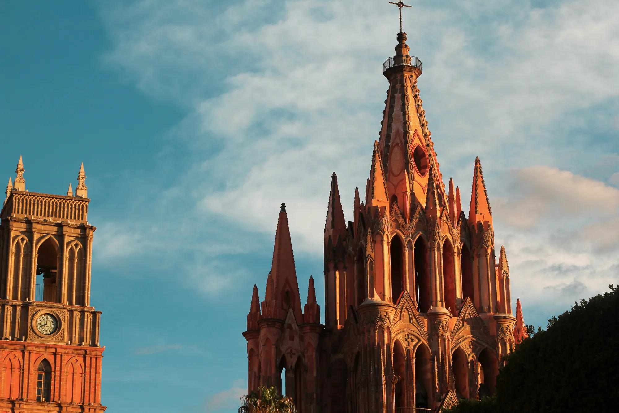The upper part of the Parroquia de San Miguel Arcángel, with its pointed spires silhouetted against a clear blue sky.