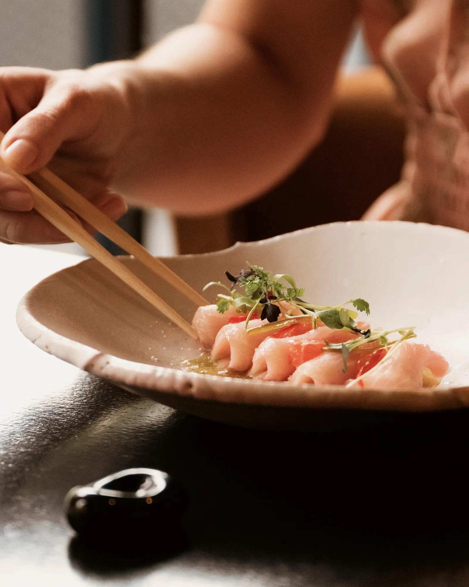 A guest using chopsticks to grab hamachi ceviche from the plate