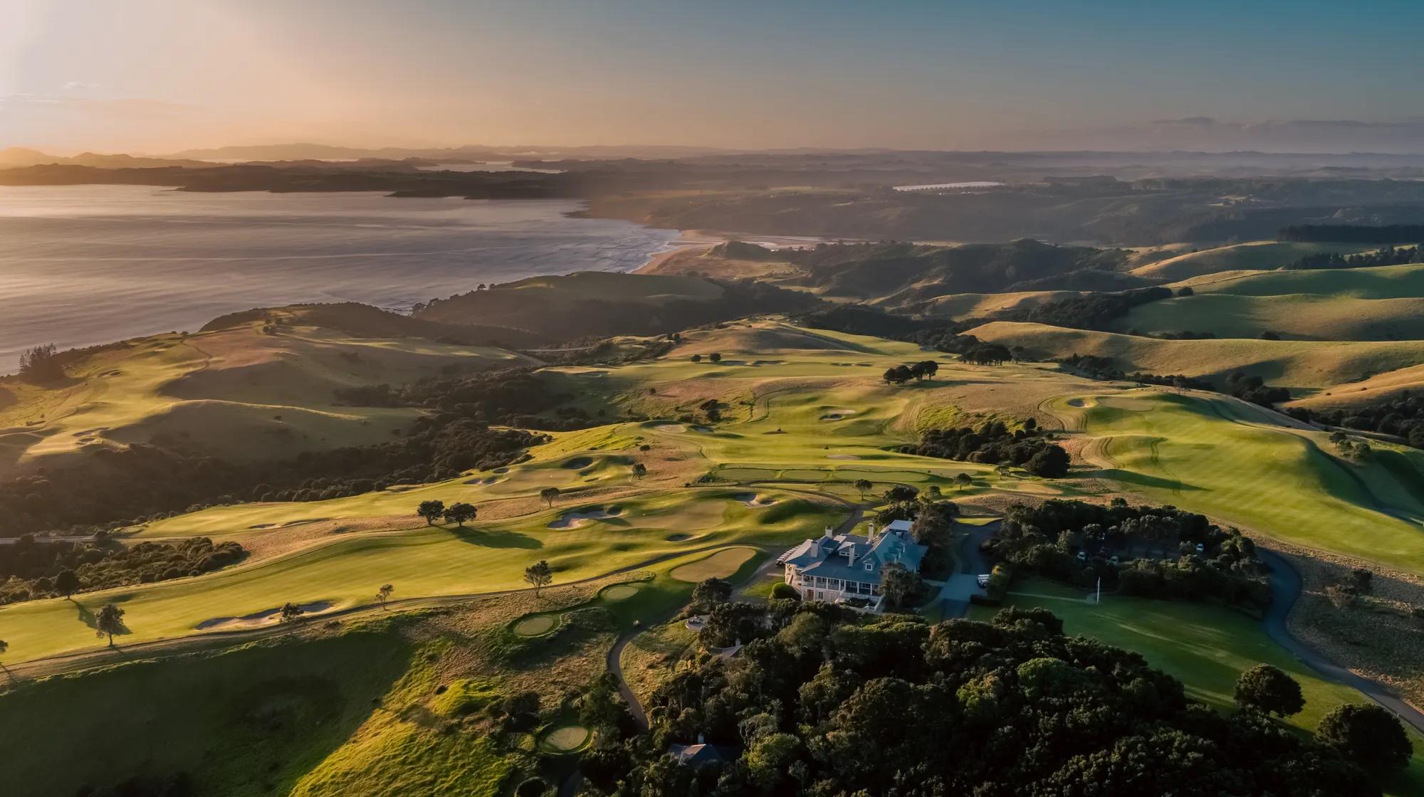 Wide aerial shot of Kauri Cliffs golf course and Rosewood Kauri Cliffs lodge building, at sunset