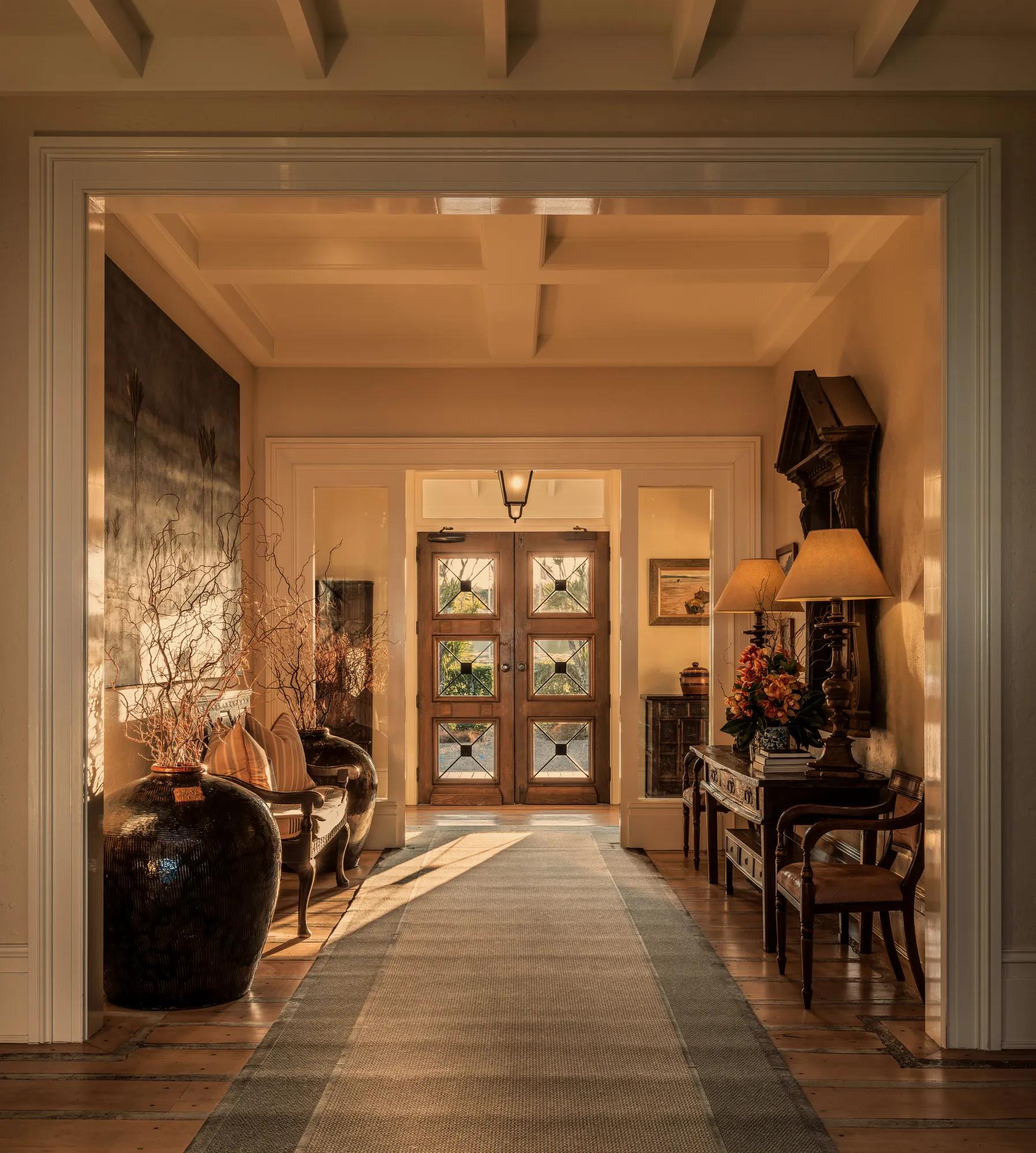 Sun streaming in the glass doors of a grand entry of a luxury lodge, elegant furnishings and artwork.