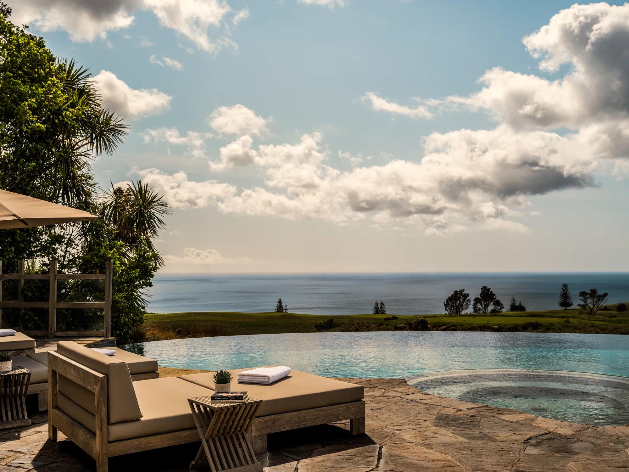 Infinity pool and jacuzzi at a luxury hotel with sun loungers and panoramic views of a golf course and out to the Pacific Ocean.