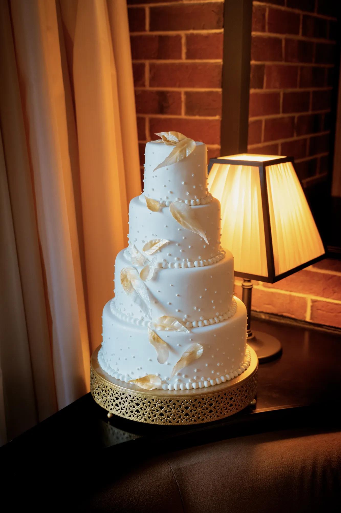 A wedding cake with intricate designs and airbrushed feathers in front of warm lighting against a brick wall.