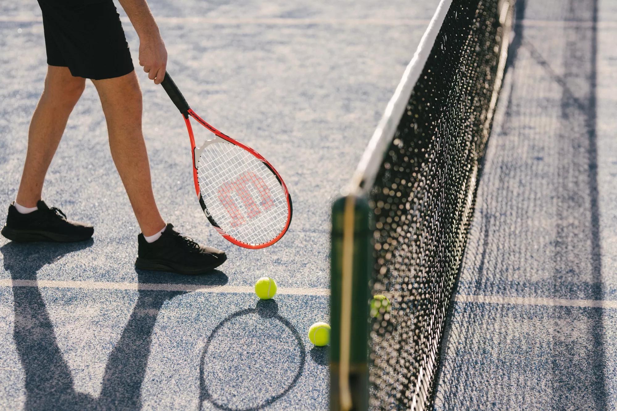 Person picking up a tennis ball with a racquet