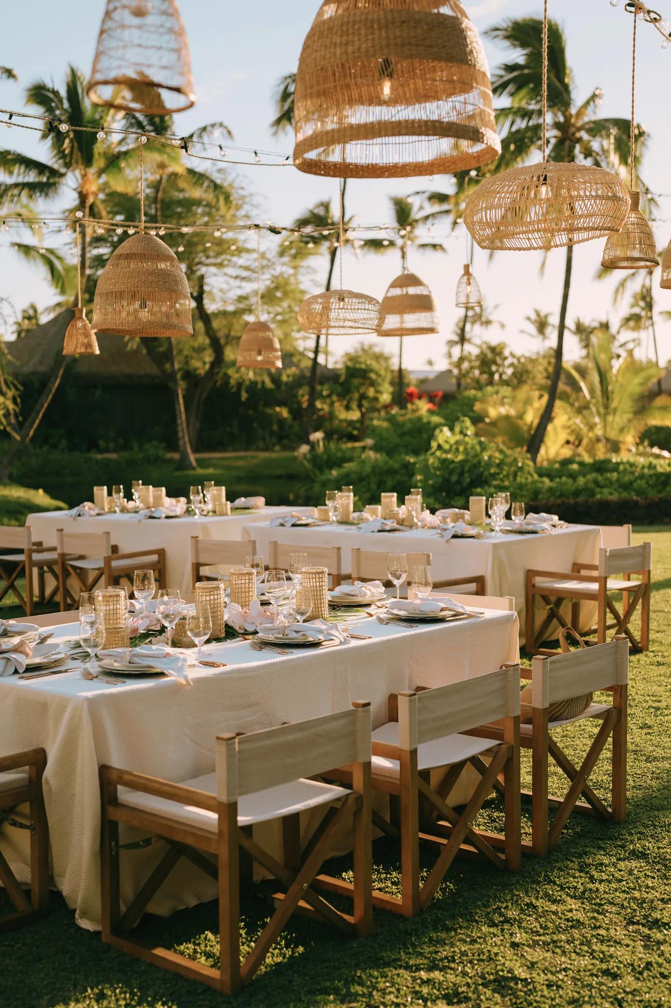 Table set for an event on a lawn with string lights and rattan lanterns 
