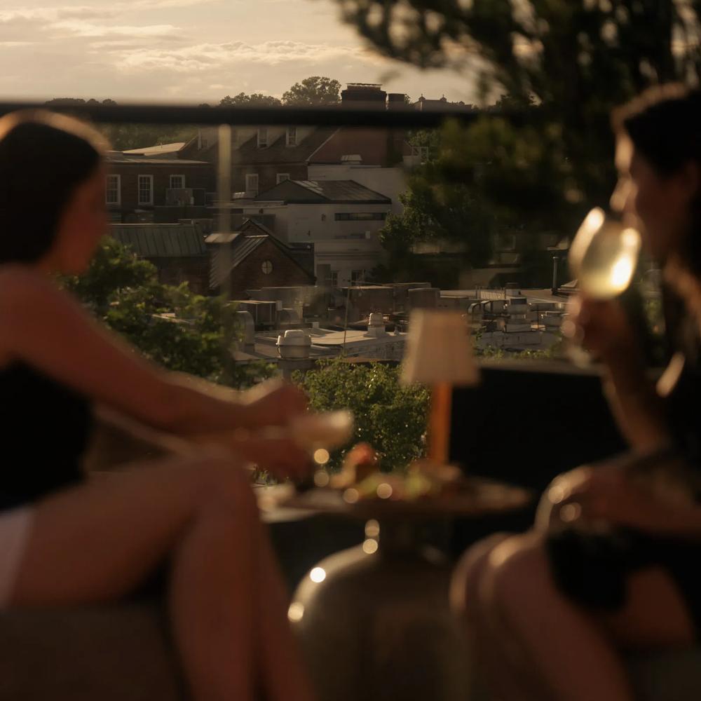 Two guests enjoying dishes and beverages on a rooftop in the heart of Georgetown as the sun is setting.