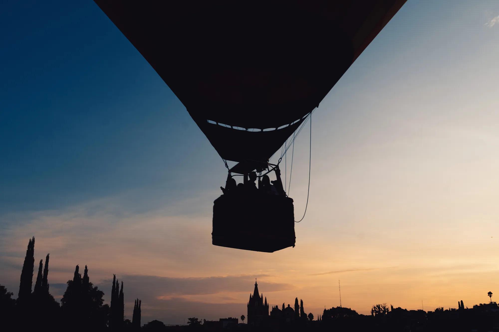 Hot air balloon basket with passengers soaring at sunset, overlooking the scenic landscapes of San Miguel de Allende.