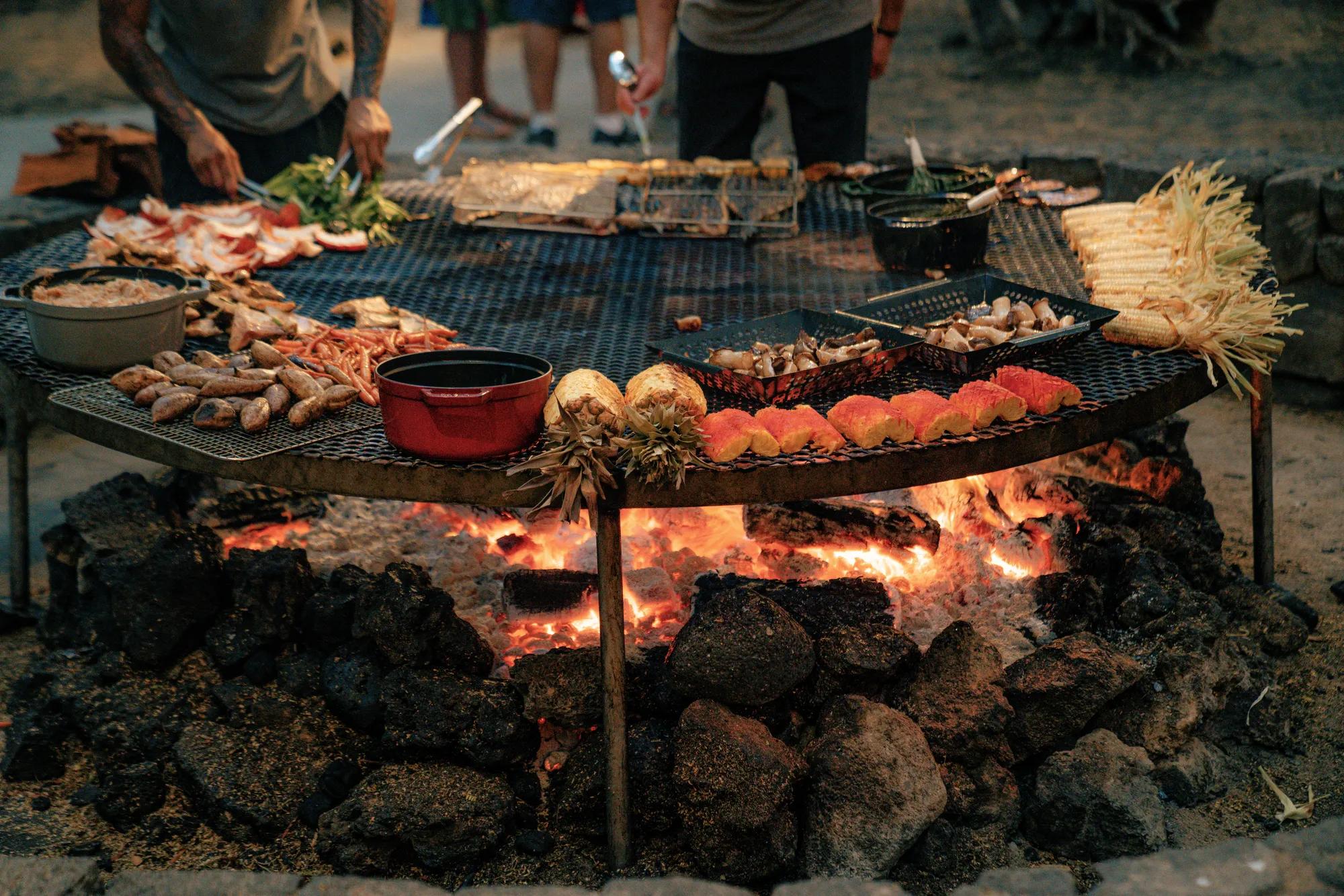 Meat and produce cooking on an open in ground grill