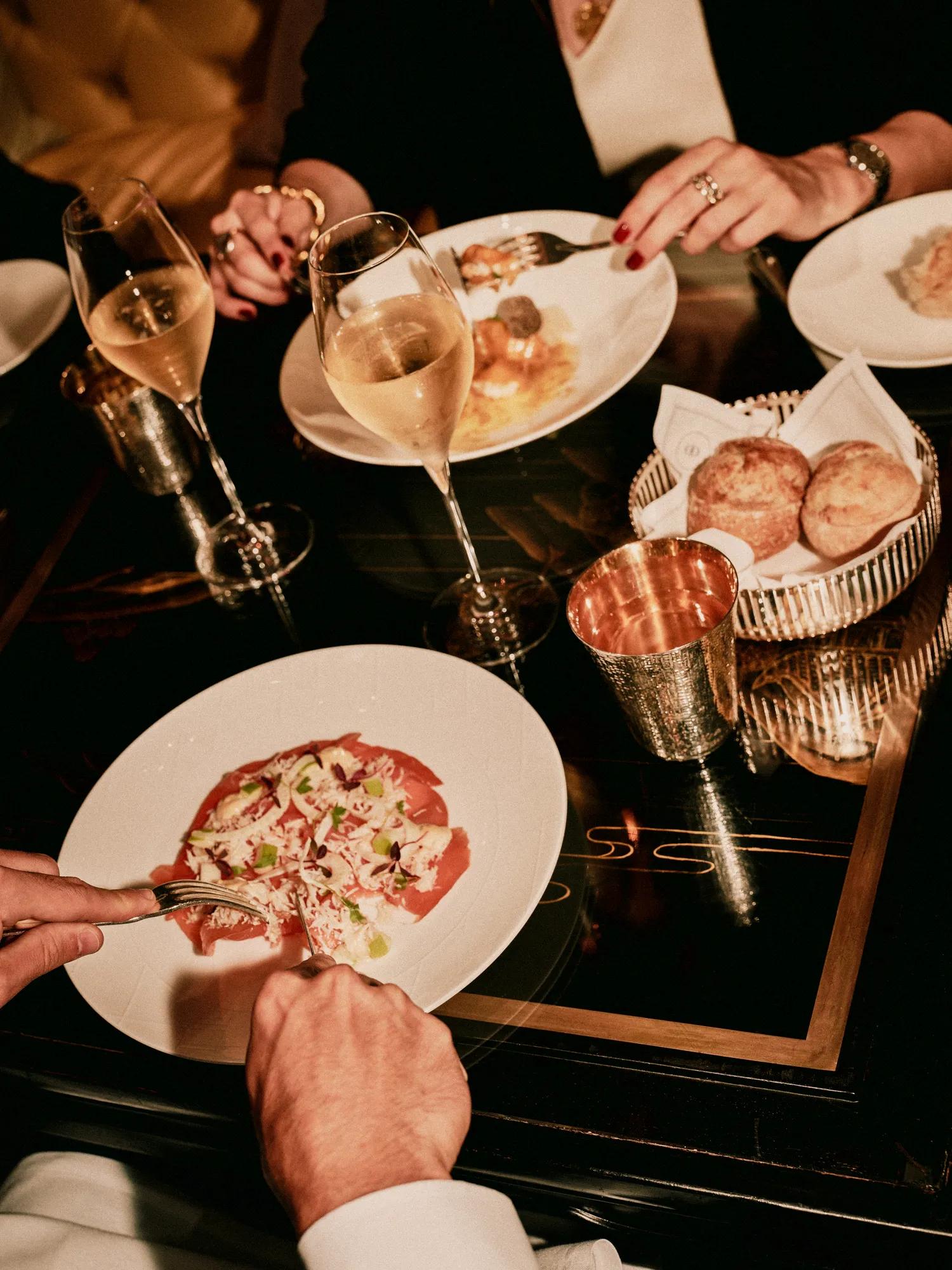 Guests enjoying champagne and sharing dishes at a candlelit dining table at Rosewood London.