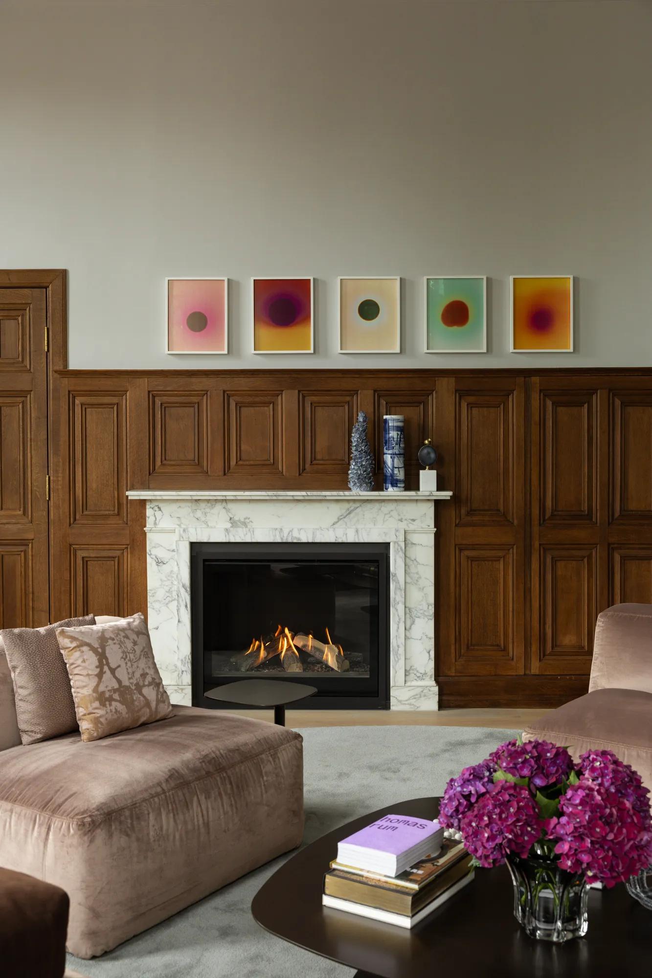Room with wood paneling and marble fire place with two velvet chairs and coffee table