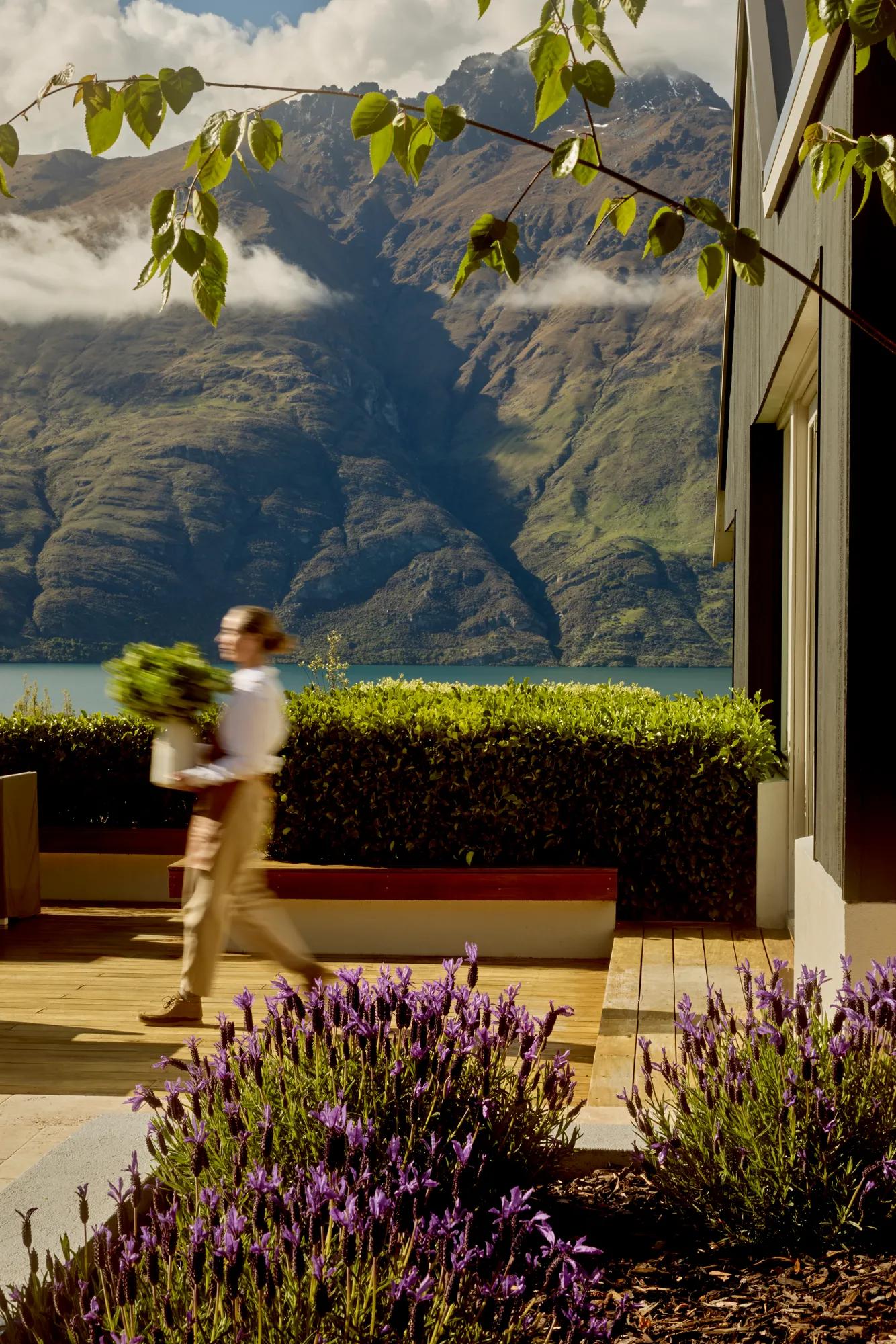Florist carries a vase full of flowers across the Remarkables Terrace at Rosewood Matakauri.