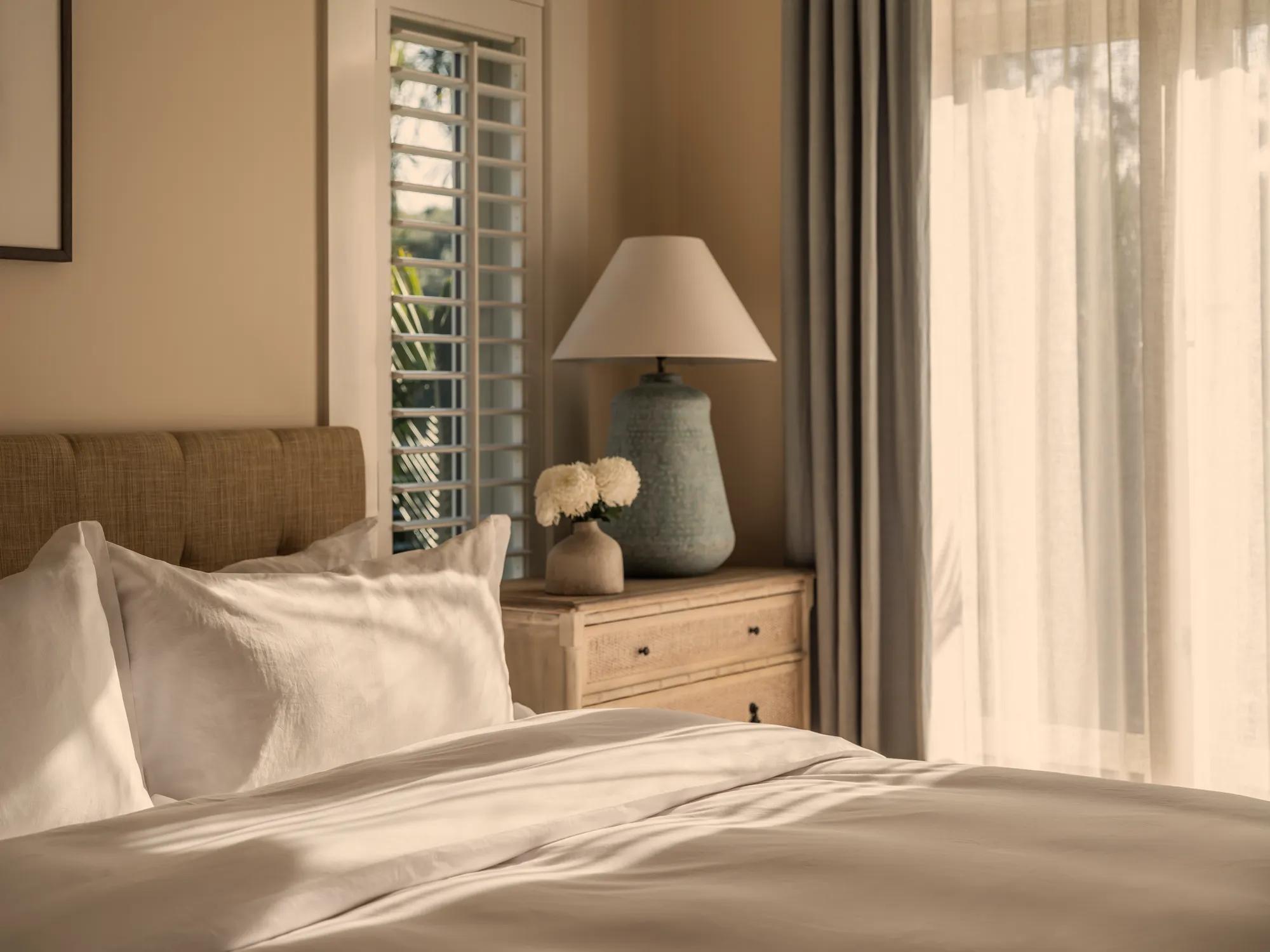 Luxury hotel bedroom with turndown service, plush white bedding, sun shining in, and a cosy, relaxing ambiance.