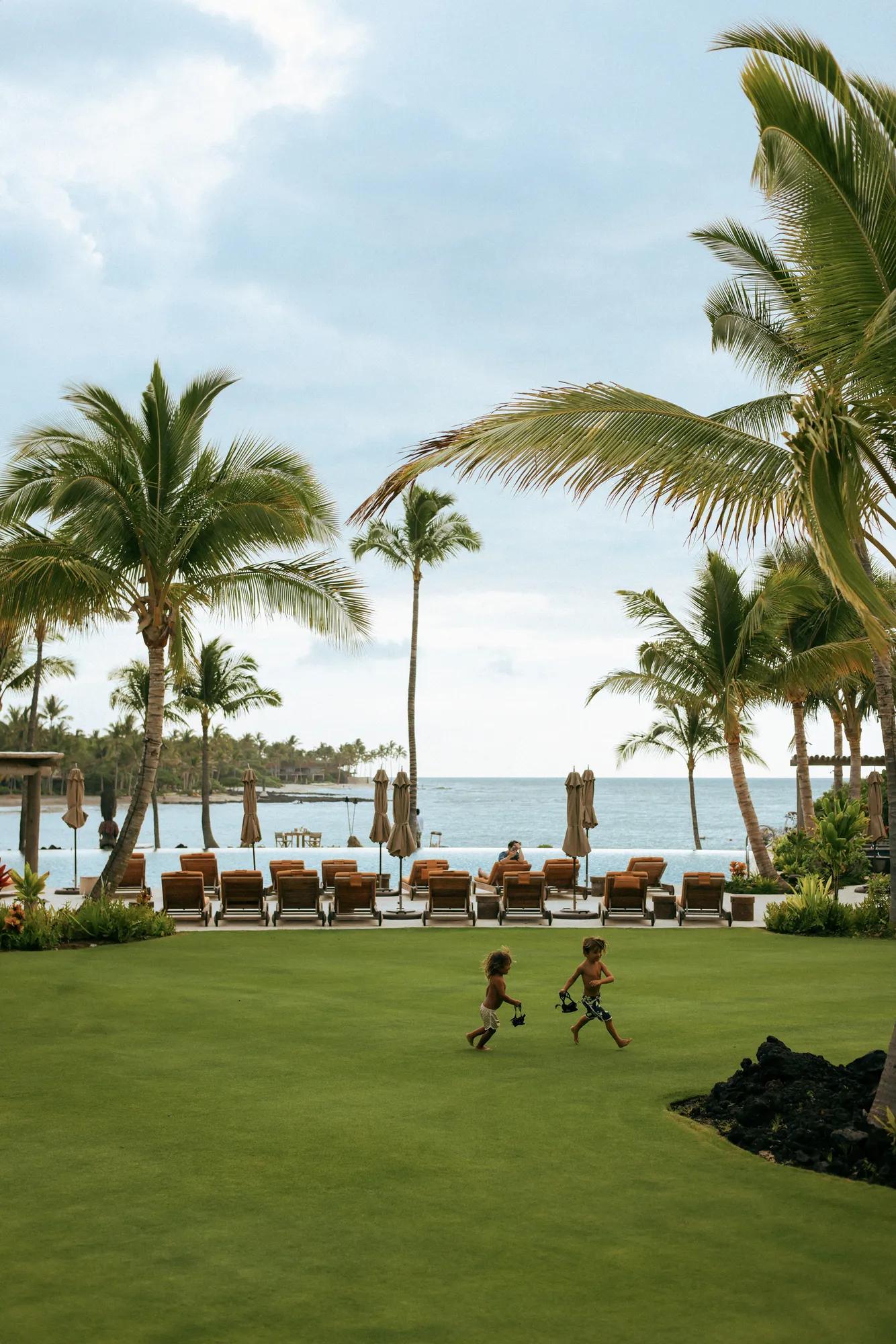  Open lawn with pool, loungers, and ocean in the distance with two little boys running and playing