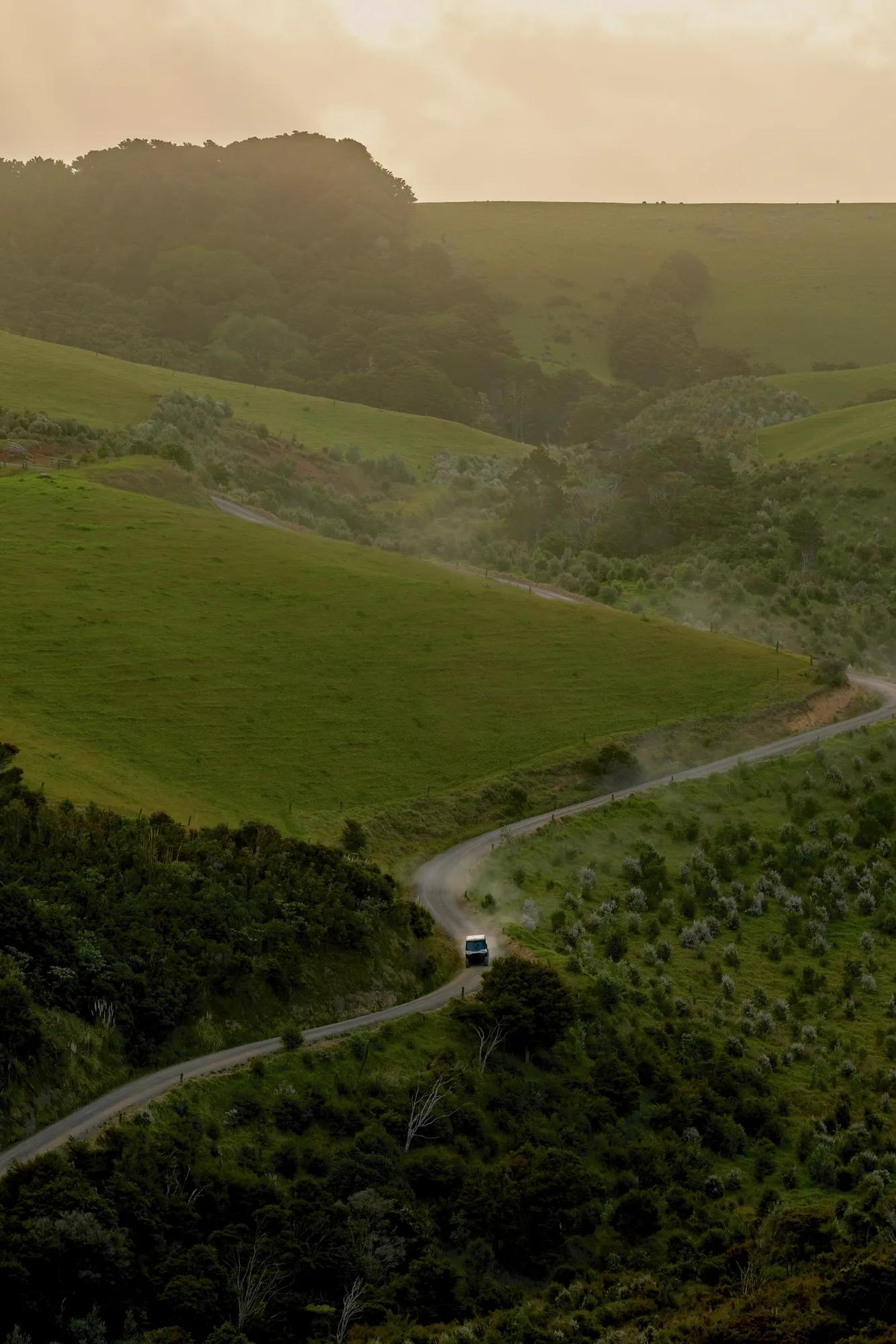 Can-Am ATV vehicle travels down a secluded road surrounded by native bush and rolling green hills