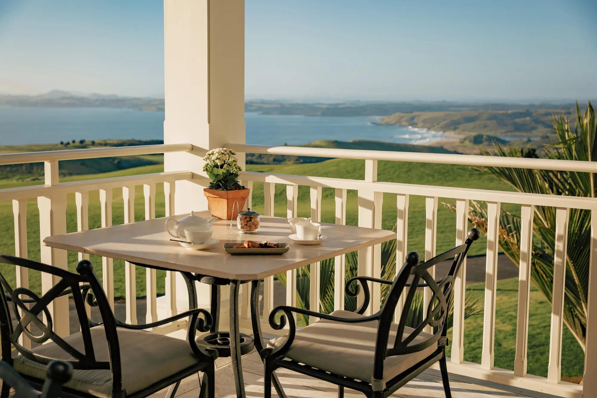 Tea set up on an outdoor table set on a balcony overlooking a golf course and the coast.