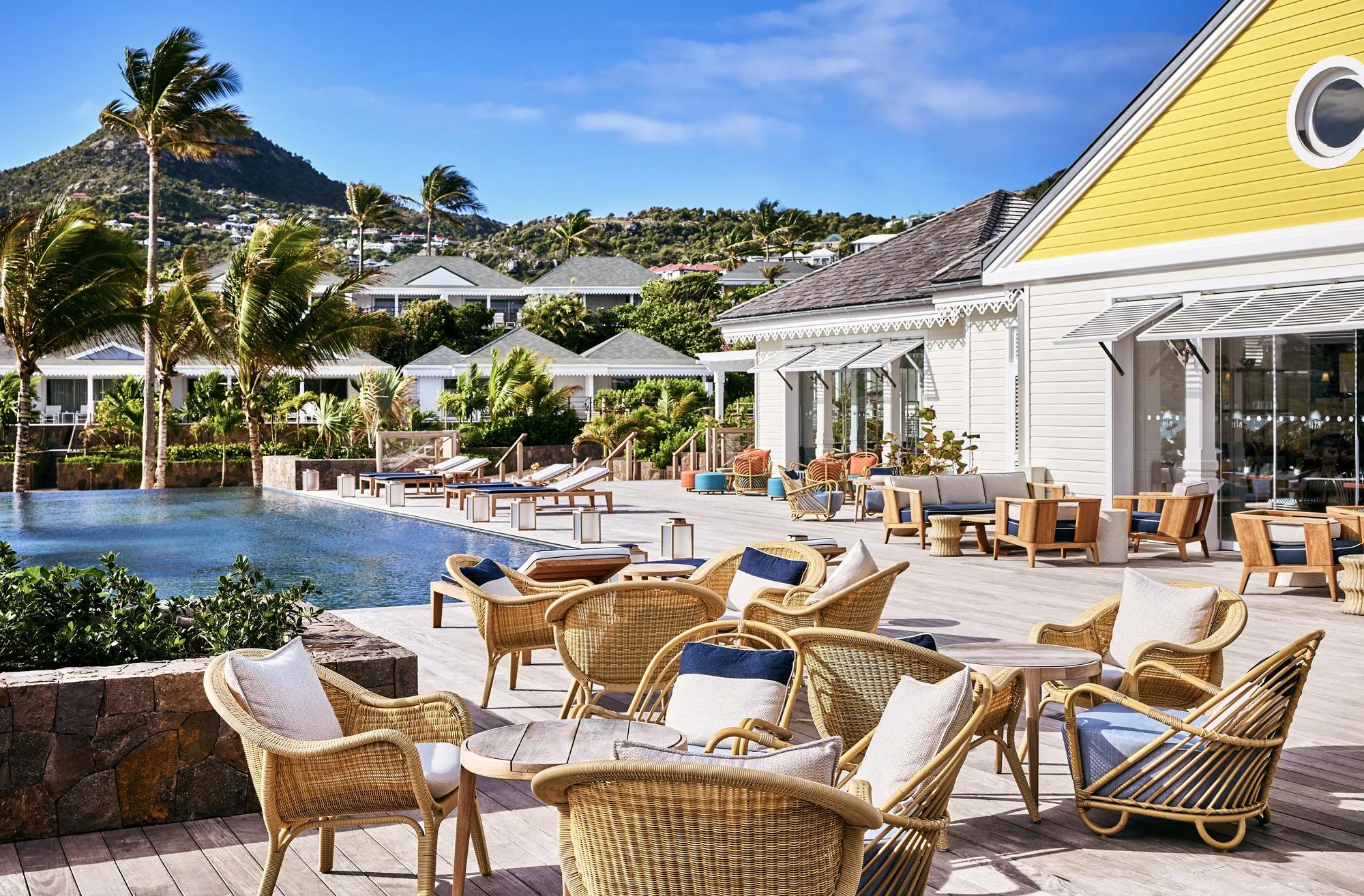 A daytime view of a poolside setting featuring wicker chairs, tables, and palm trees.