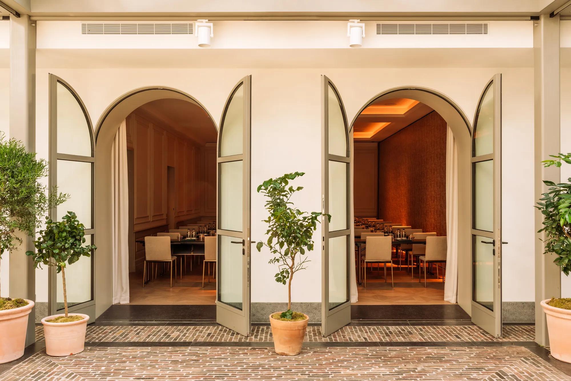Two arched doorways open from a grand ballroom into a brick courtyard flanked by potted orange and lemon trees. 