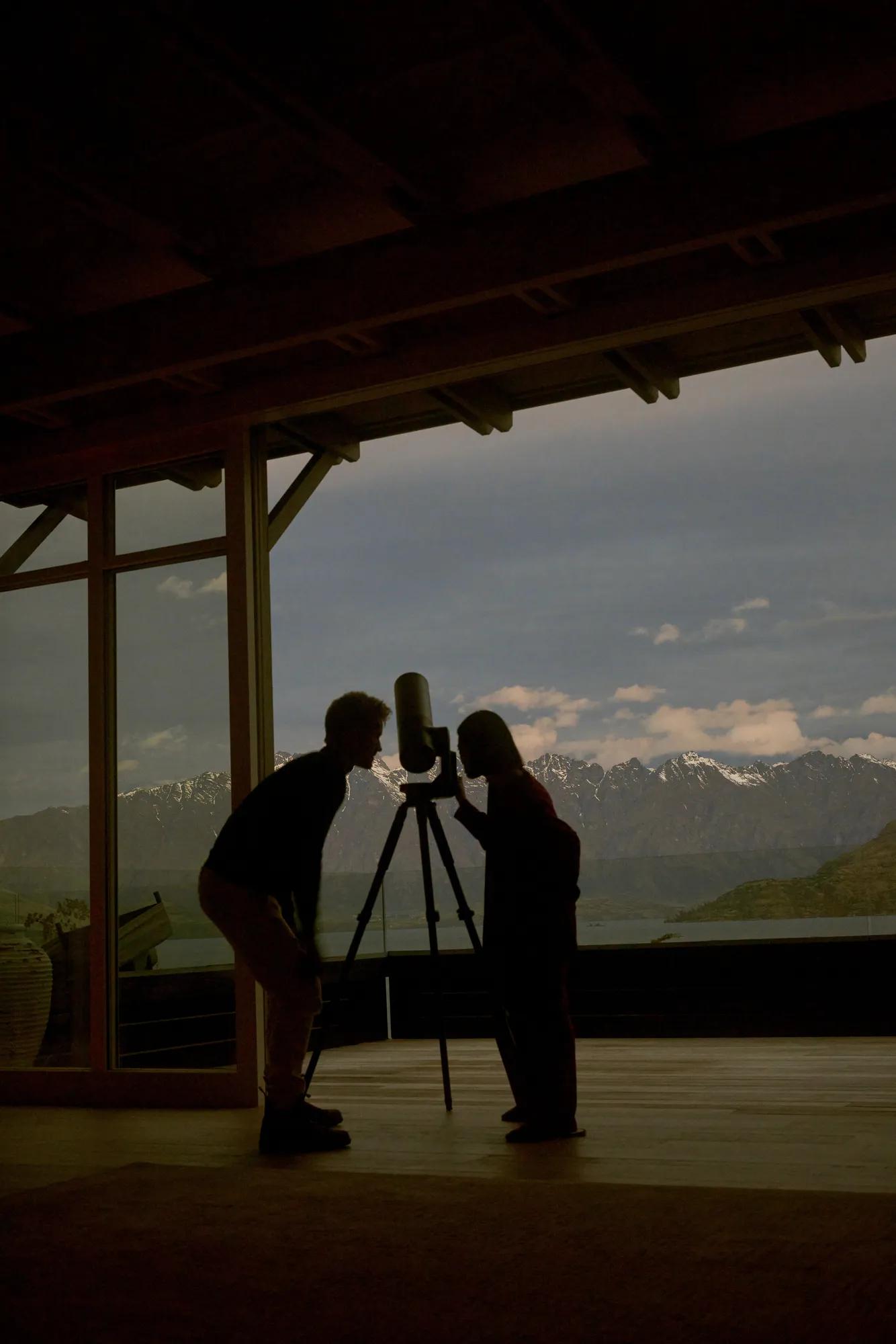 A couple look into a telescope set up to admire the Southern night sky on the balcony of the Matakauri Four Bedroom Villa.