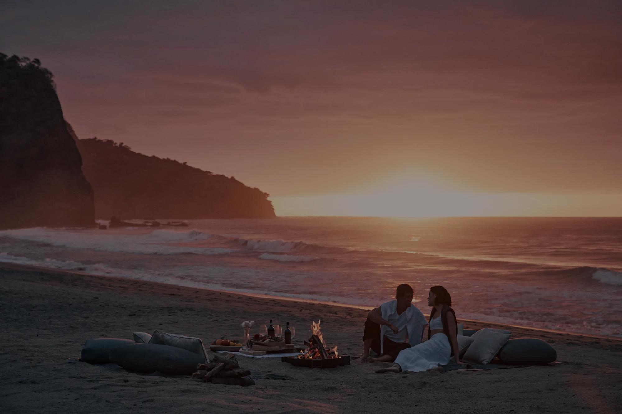 Couple enjoying a romantic dinner on the beach at sunset, with ocean views and warm golden light