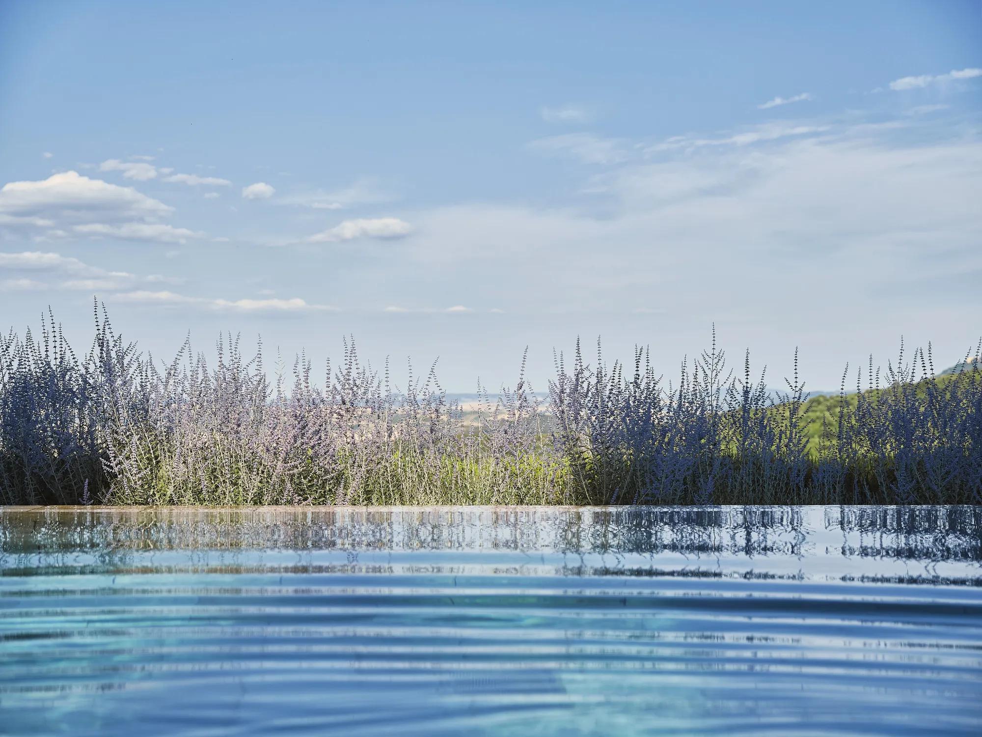 Infinity pool with view over the Val d’Orcia hills and blue sky.