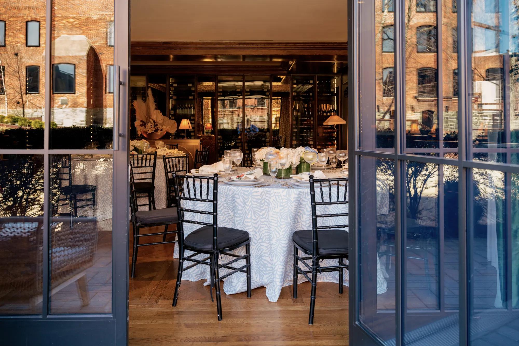 Looking through open patio doors at the CUT Bar & Lounge with round tables featuring patterned linens and colorful place settings.