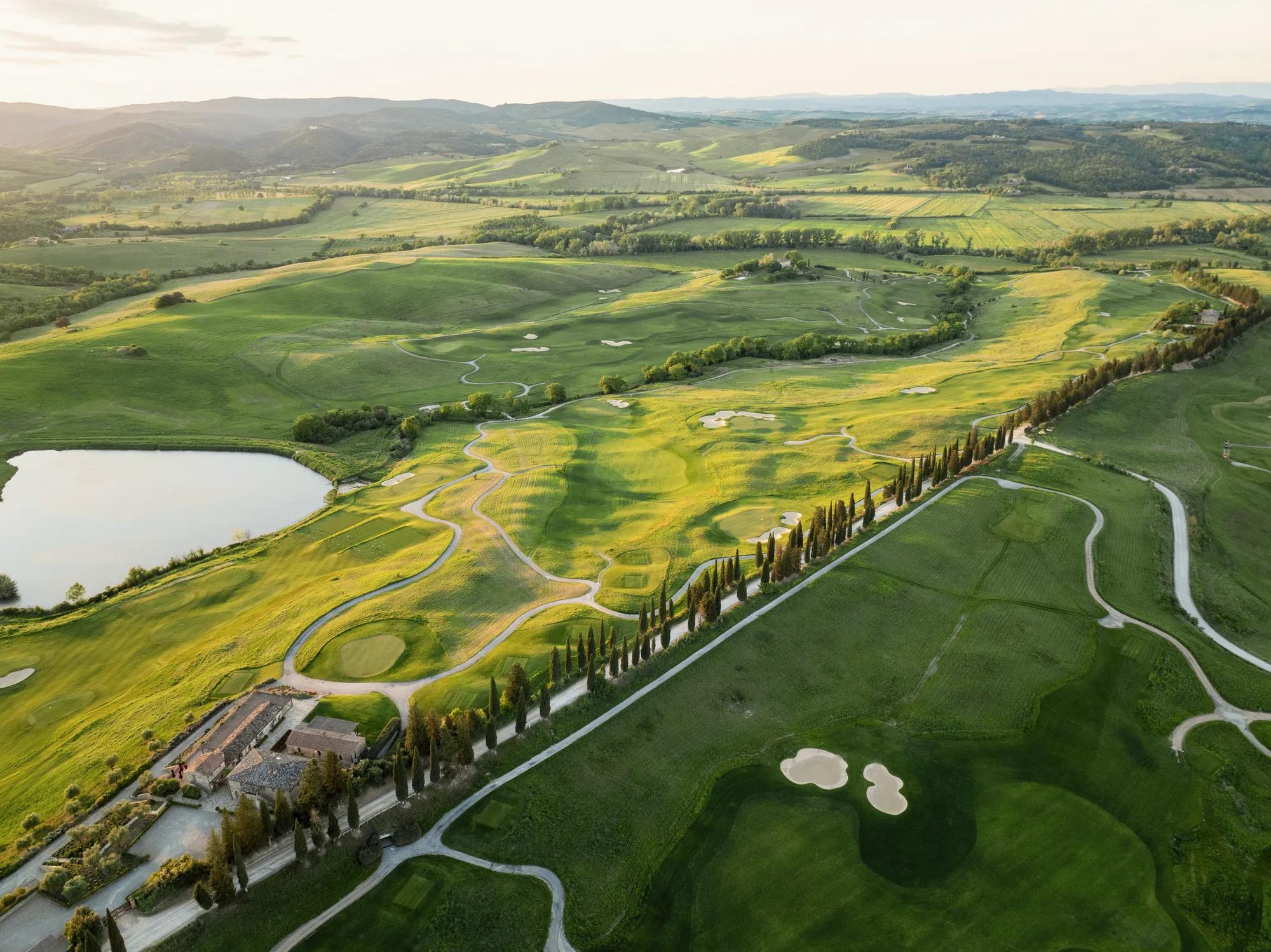 A golf course surrounded by mountains with a  long road in the middle.