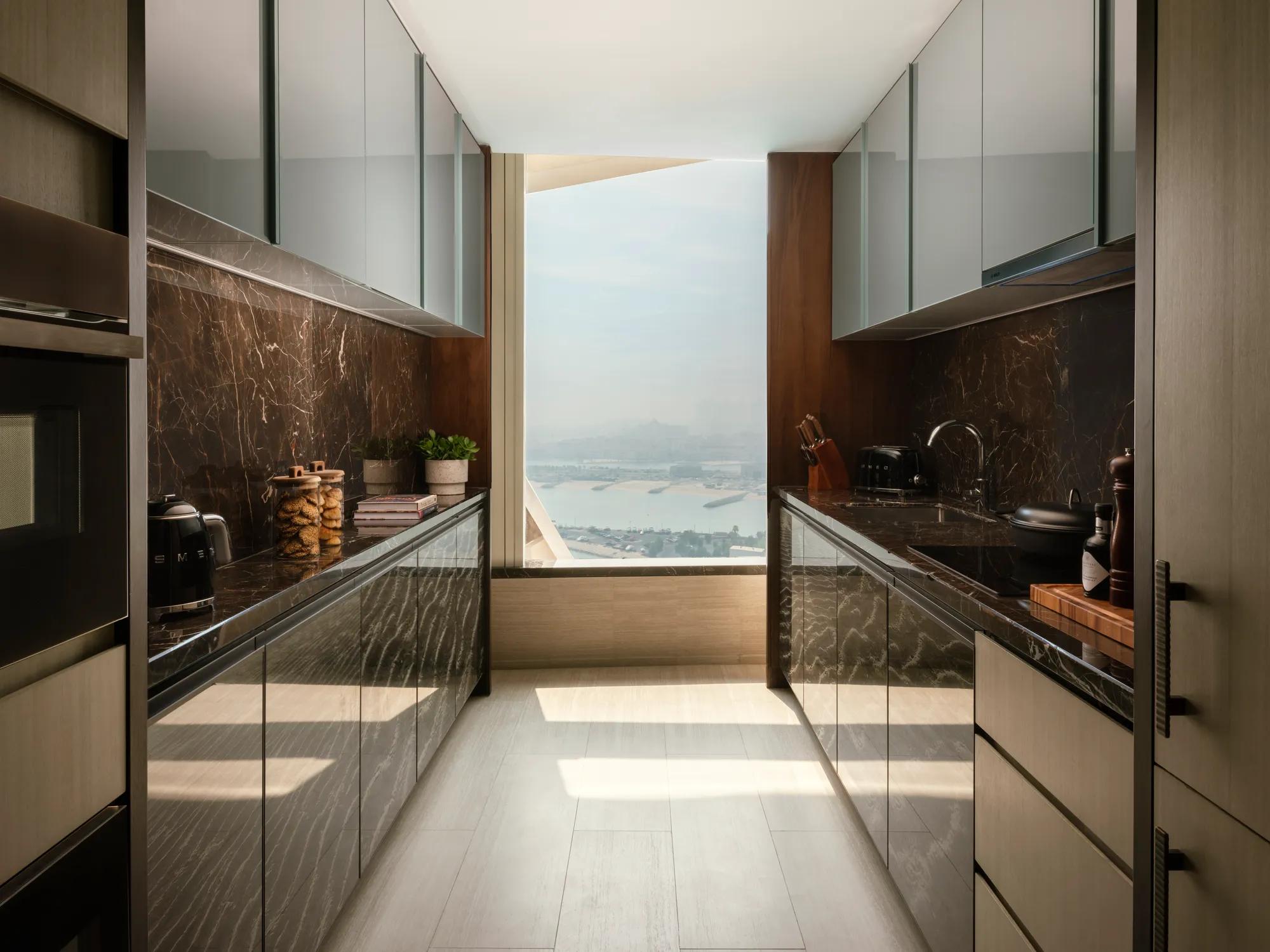 Sleek galley kitchen with dark marble backsplash and glossy cabinetry, featuring a large window at the end providing a panoramic city view.