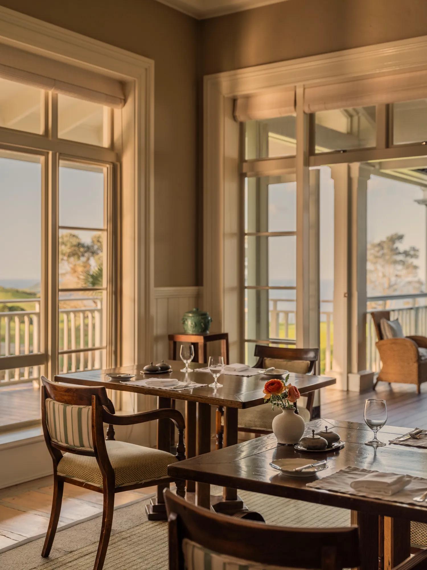 Dining room with beautifully set tables opening to a covered balcony with panoramic ocean views.